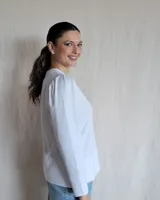 Remera blanca de manga larga con diseño de cuello en V y detalle de tablas frontales. Presenta mangas con sutil frunce en los hombros y puños rectos.