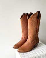 Bota estilo tejana de cuero vacuno color tostado, con costuras decorativas en contraste en la caña y taco bajo.