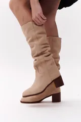 Bota de caña alta color beige, confeccionada en cuero gamuzado. Tiene taco de madera y puntera redondeada.