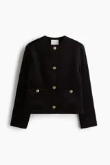 Chaqueta de pana negra con cuello redondo, cierre frontal de botones dorados y dos bolsillos tipo parche en la parte delantera.