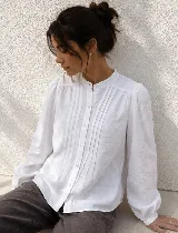 Camisa blanca de corte clásico con cuello mao y cierre frontal de botones. Presenta mangas largas con puños elásticos y detalles de tablas verticales en el frente.