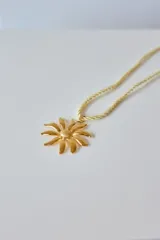 Collar con tiento trenzado blanco y dije metálico dorado con forma de sol estilizado.