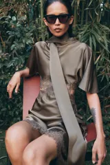 Vestido midi satinado de cuello subido y manga corta tipo capa. Presenta aberturas laterales con aplicación de encaje a tono y bajo asimétrico con detalle de encaje. Incluye un pañuelo integrado en el mismo tejido y cierre posterior con botones forrados.