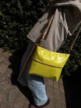 Cartera bandolera de cuero flexible color amarillo, con trenza artesanal al frente, interior forrado y correa larga con herrajes de metal.