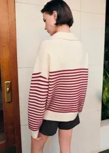 Chaleco de punto color marfil con cuello polo, escote en V y diseño de rayas horizontales burdeos en el pecho y las mangas. Cuenta con mangas largas y un diseño holgado, ideal para usar superpuesto o anudado.