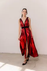 Vestido largo de seda color bronce con acabado brillante, escote profundo en V y espalda abierta. Presenta detalles en terciopelo negro que enmarcan el escote, recorren el frente y definen la cintura con una faja ajustable. Posee breteles anchos y una abertura frontal en la falda.