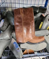 Bota de cuero marrón con diseño 2 en 1, que incluye una polaina desmontable. Presenta una caña alta estructurada y una base de bota tipo botineta con suela plana de goma negra.