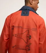 Campera rompevientos azul marino con capucha, cierre frontal y bolsillos laterales. Presenta estampado de NASA en el pecho, parche de bandera estadounidense en la manga y bolsillo utilitario en el brazo.