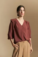 Camisa negra de manga larga con escote en V y cierre frontal de botones. Presenta detalles de volados en los hombros, frunces en la espalda y puños elastizados que le otorgan una silueta relajada y fluida.