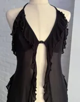 Top halter negro de microtul transparente, con escote en V profundo y bordes con volados o festones. Presenta un cierre frontal central.