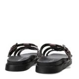 Sandalias planas Miss Carol modelo Nevada, color marrón, con tres tiras en el empeine decoradas con tachas metálicas plateadas. Una de las tiras cuenta con una hebilla de ajuste lateral. Poseen suela y plataforma baja de color negro.