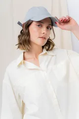 Gorra verde militar de diseño clásico con visera curva y aplique metálico plateado con la inscripción "Peach" en el lateral frontal. Cuenta con tira ajustable en la parte trasera.