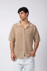 Camisa de punto calado en color beige, de manga corta y corte relajado. Presenta cuello tipo bowling, cierre frontal con botones al tono y una estructura liviana y respirable confeccionada en algodón.