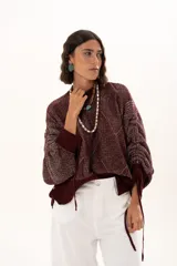 Buzo de punto color vino con diseño de trama geométrica, cuello redondo, mangas largas con puños ajustables mediante cordones y terminaciones acanaladas.