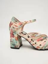 Sandalias de tacón cuadrado de 8 cm, confeccionadas en charol color crema. Presentan un diseño de tiras finas entrelazadas en la parte frontal y una correa ajustable con hebilla metálica en el tobillo.