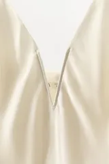 Top lencero de satén color beige, con escote en pico profundo con abertura central y tirantes finos.
