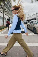 Camisa de popelín celeste con cuello solapa y manga larga, combinada con un chaleco de punto trenzado en color azul marino superpuesto. Presenta un diseño de capas con cierre en la espalda mediante botones ocultos.