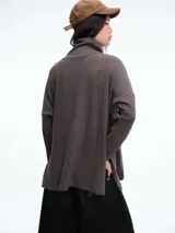 Buzo tejido de silueta holgada en color beige, con cuello alto y mangas largas. Presenta tajos laterales en el ruedo que aportan movimiento a la prenda.