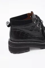 Borcego de cuero color gris con cordones color naranja, suela track negra de goma y detalle de gamuza en la parte superior del tobillo.