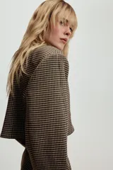 Blazer corta de corte recto con estampado de cuadros pequeños en tonos marrones y negros. Presenta cuello solapa, manga larga y cierre frontal con un botón.