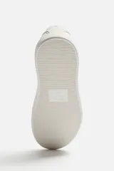 Zapatilla blanca de cordones fabricada en tejido transpirable de punto, con horma redonda y suela a tono.