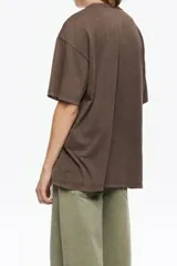 Camiseta de algodón orgánico color negro con efecto gastado, corte oversize y manga corta ancha. Presenta un estampado artístico enmarcado con el texto "BIMBA Y LOLA" en la parte superior e inferior.