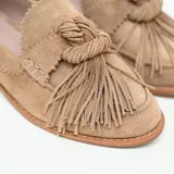 Mocasines de gamuza color marrón claro, con taco bajo, lengüeta con flecos y detalle de nudo frontal.