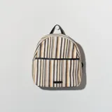 Mochila pequeña con estampado a rayas verticales en tonos blanco, marrón, gris y amarillo. Tiene un bolsillo frontal con cierre y detalles en cuero sintético negro, incluyendo el asa superior y el logo frontal.
