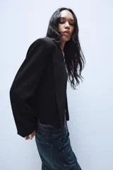 Blazer corto de corte recto con cuello de solapa, manga larga y hombreras. Presenta un diseño minimalista sin botones y forro interior a tono.
