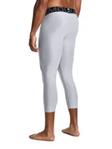 Calza deportiva de compresión tipo 3/4, color gris claro, con cintura elástica ancha negra con logo de la marca. Presenta paneles de malla para ventilación, bolsillo lateral y logo de Under Armour en la pierna.