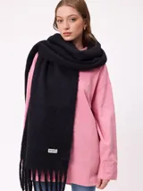 Bufanda de tejido suave con diseño de cuadros grandes en tonos naranja, rojo, violeta y lila. Presenta flecos en los extremos y una etiqueta pequeña con el logo de la marca Rusty.