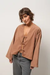 Blusa marrón de corte crop, escote en V y mangas largas anchas. Cierre frontal con lazos.