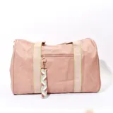 Bolso tipo duffel color rosa con textura símil cuero, doble asa corta y correa larga desmontable. Tiene un bolsillo externo con cierre y un charm colgante con diseño geométrico.