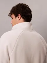 Buzo polar de Calvin Klein en color beige, con cuello alto tipo mock neck y cierre de media cremallera frontal. Presenta un diseño de corte regular con mangas largas, bajo ajustable con cordón y logo de la marca bordado en el pecho.