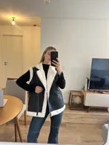 Chaleco negro con cuello solapa y borde de piel sintética, cierre frontal con cremallera y bolsillos laterales con cremallera.