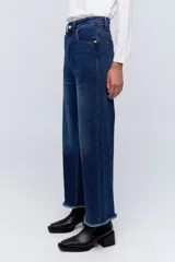 Jean de pierna ancha, tiro alto, color azul oscuro con desgaste en los muslos y ruedo desflecado.