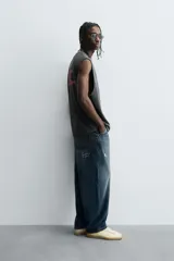 Sudadera sin mangas (tipo chaleco) de color gris oscuro con efecto lavado, corte relajado y cuello redondo. Presenta un estampado frontal en color rosa neón con texto y gráficos abstractos.