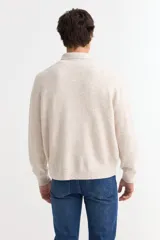 Sweater de punto color beige con cuello polo, cierre frontal parcial y bolsillo en el pecho. Presenta mangas largas con puños acanalados y diseño de corte recto.