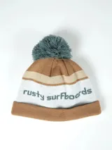 Gorro de lana Rusty Balve con diseño de franjas en tonos marrón, beige y blanco, puño vuelto marrón y pompón superior verde. Cuenta con la inscripción 'rusty surfboards' bordada en el frente.