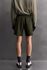 Bermuda de hombre color verde militar, de corte regular fit, confeccionada en tejido técnico compacto con elasticidad. Presenta cintura ajustable con cinturón a contraste, bolsillos frontales y un bolsillo plastrón con cierre de cremallera oculta en una de las perneras.