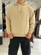 Canguro oversize beige con capucha y cordones ajustables, bolsillo tipo canguro y pequeño bordado en el pecho.