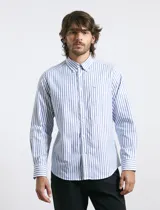 Camisa de corte clásico confeccionada en tejido oxford, con diseño de rayas verticales en tonos azul y blanco. Presenta cuello abotonado, cierre frontal con botones y bolsillo en el pecho con detalle de etiqueta bordada.