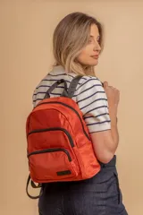 Mochila urbana de diseño funcional en color beige, confeccionada en tela impermeable. Cuenta con un compartimento principal amplio, un bolsillo secundario y un bolsillo frontal, todos con cierre. Incluye asa superior y correas ajustables para los hombros, con detalle de etiqueta de marca en el frente.