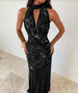 Vestido largo negro con cuello halter y escote pronunciado en V. La parte superior está decorada con un patrón de pedrería brillante, y la falda es lisa y fluida.