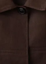 Chaqueta de lino color marrón, de diseño recto, manga larga, cuello camisero, cierre frontal de botones y cinturón ajustable del mismo tejido.