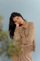 Camisa de lino color tostado con cuello clásico y cierre frontal de botones. Presenta detalles de encaje crochet en los puños y en el ruedo inferior.