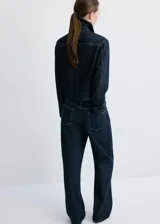 Chaqueta de denim azul oscuro, de corte corto (cropped), cuello clásico, cierre frontal con botones, manga larga y un bolsillo aplicado en el pecho.