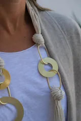 Collar largo de diseño artesanal compuesto por múltiples cordones de algodón en color crudo, entrelazados con aros y eslabones metálicos en tono dorado mate.