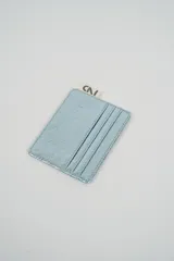 Tarjetero de cuero sintético con acabado metalizado celeste claro, con múltiples ranuras para tarjetas y un pequeño tag de tela con el logo 'CNI' en la parte superior.