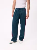 Pantalón tipo babucha de la marca Rusty, color azul petróleo con franjas laterales en color bordó. Presenta cintura elástica con cordón ajustable y logo bordado en la pierna izquierda.